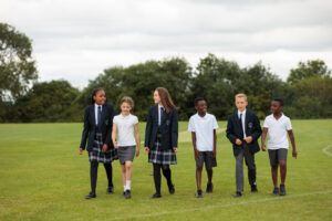 6 young children in school uniform walking in a line on a playing field